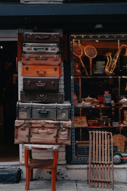 The image depicts the exterior of a furniture shop with large display windows showcasing an assortment of antique chairs, including upholstered armchairs with striped fabric and wooden-frame chairs, a